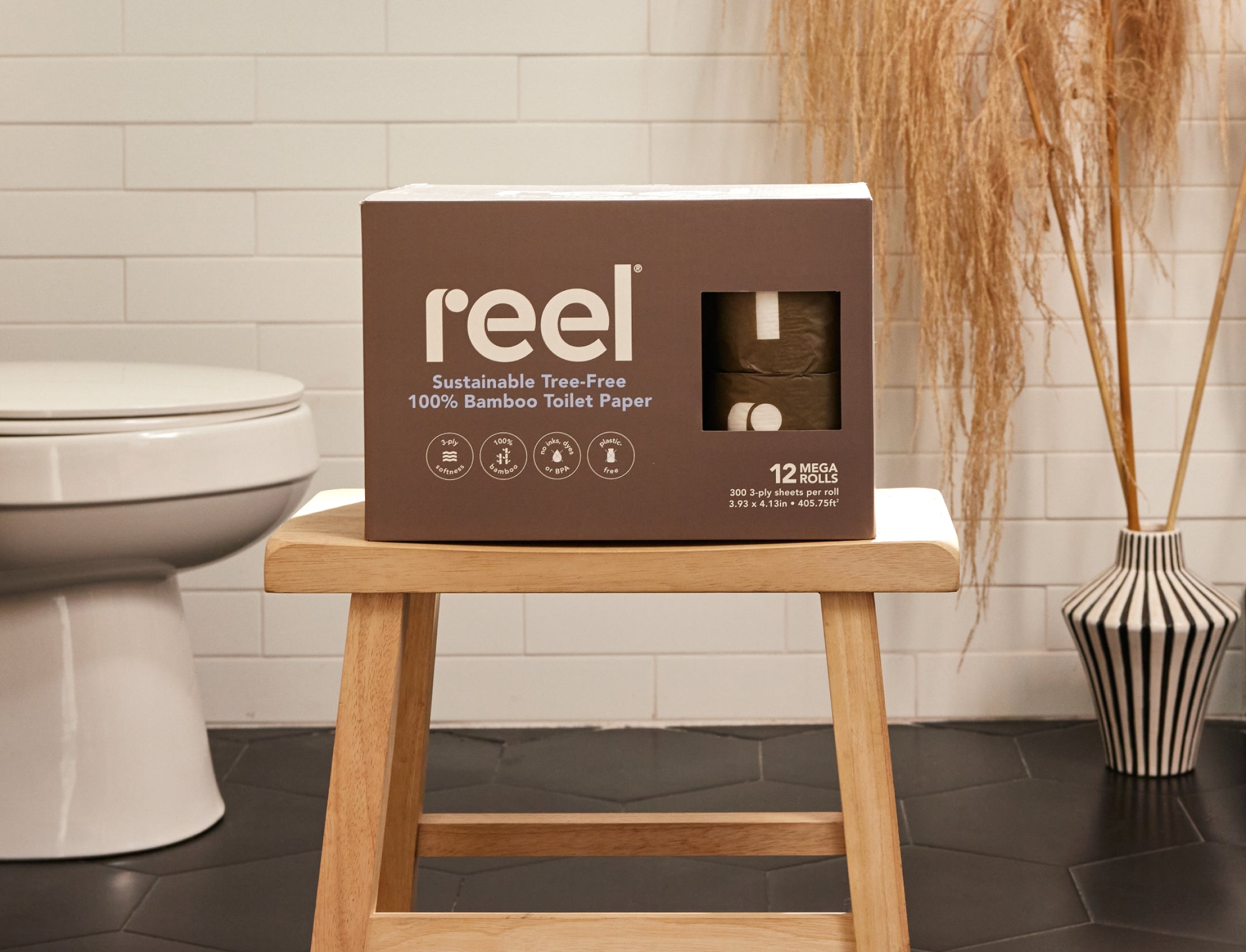 A box of Reel toilet paper sitting on a stool in a bathroom