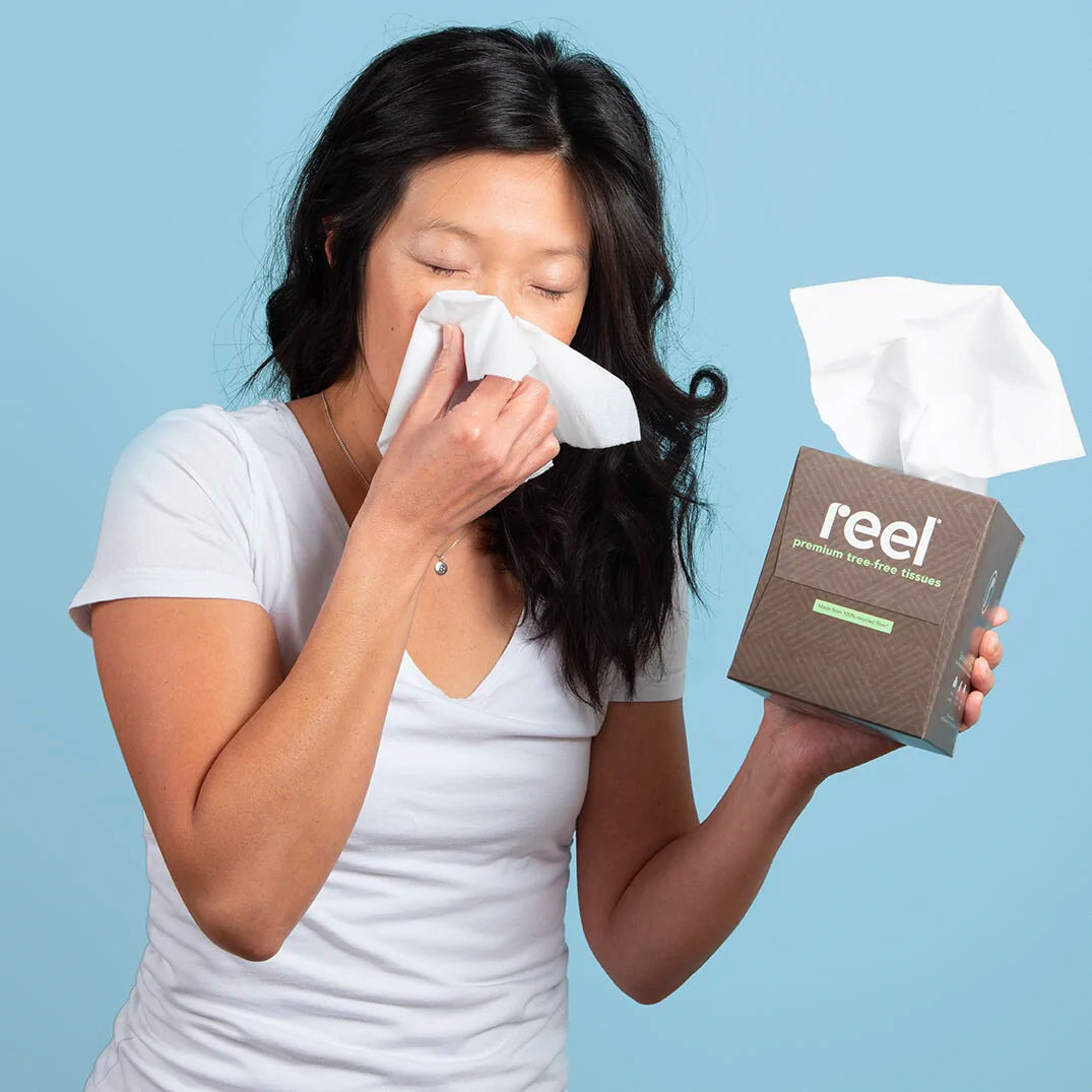 A woman blowing her noise while holding a box of Reel recycled tissues
